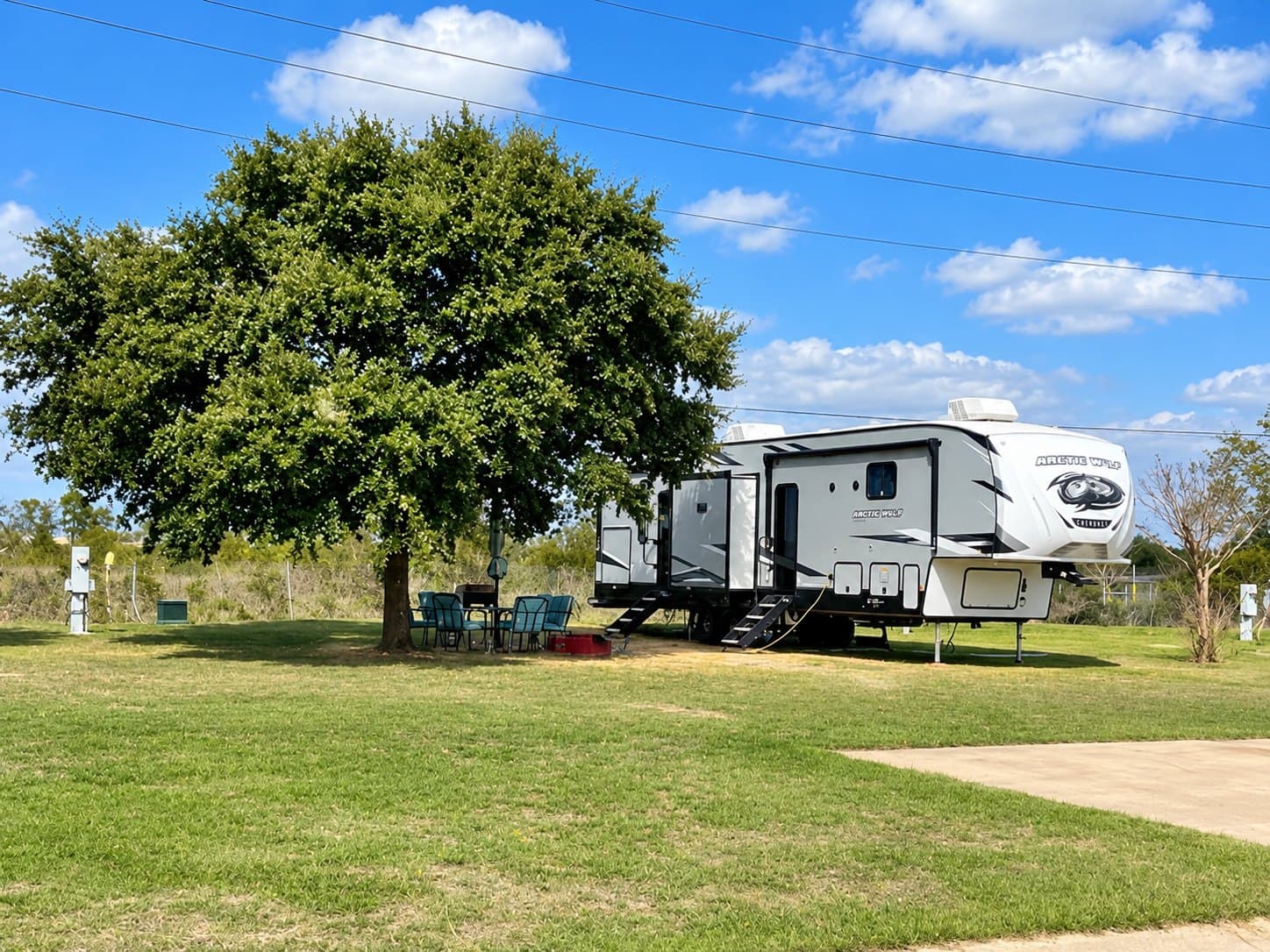 Travel trailer parked beside a large shade tree on a grass RV site at Briarwood Estates